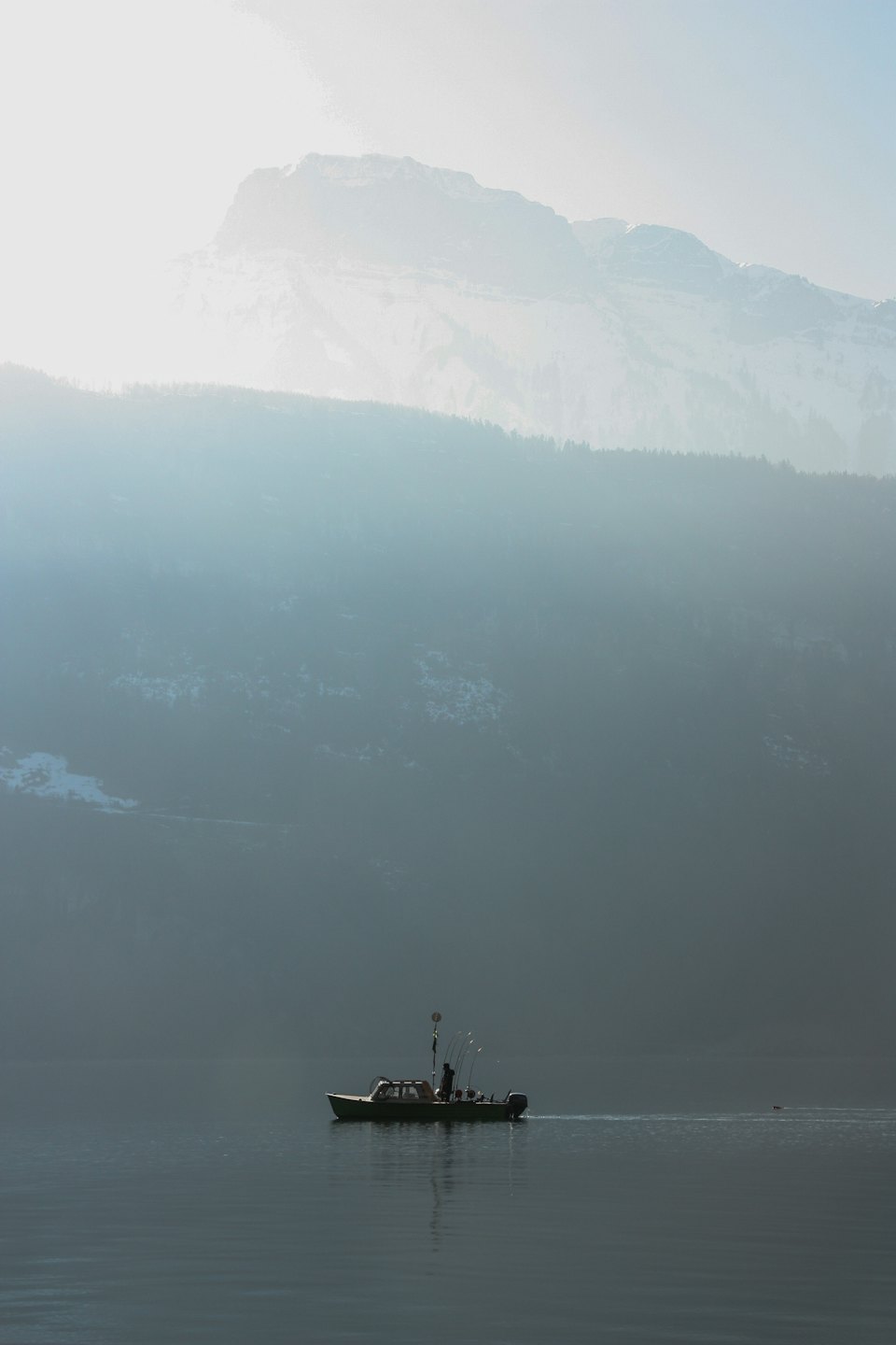 A person steers a fishing boat across a mountain lake.